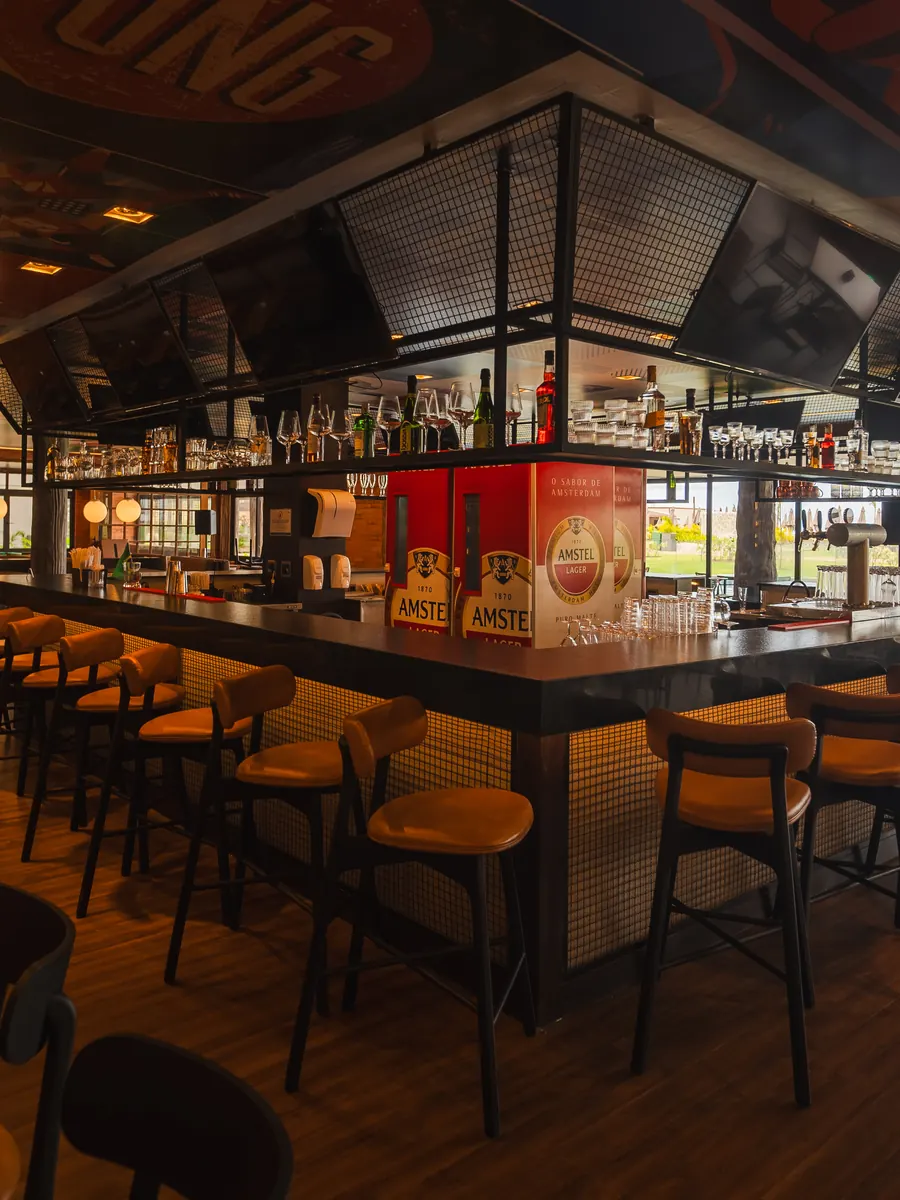 Balcão do Camarote Sport Bar, com banquetas em volta, televisores suspensos e vista para a piscina