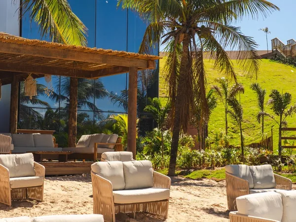Beach club do resort, com sofás de fibra na areia entre os coqueiros