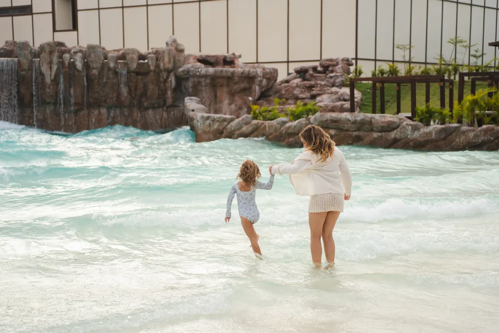 Mãe e filha de mãos dadas na piscina de ondas do resort
