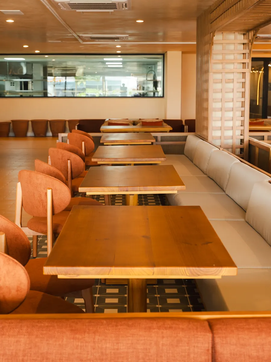 Salão do restaurante italiano Coppola, com mesas compridas de madeira e a cozinha à vista ao fundo