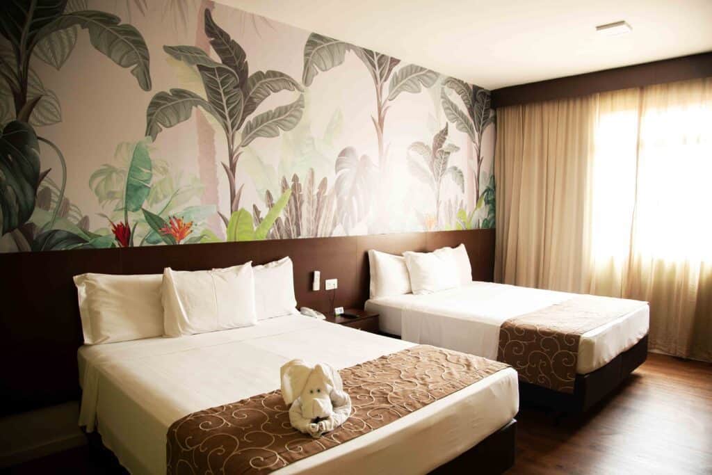 uma cama queen e uma cama de solteiro, com parede decorada com folhagens e roupa de cama branca com morrom claro.