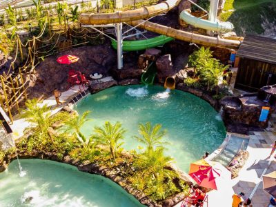 Duas piscinas separadas por um canterio de palmeiras ao centro com toboágua ao fundo.