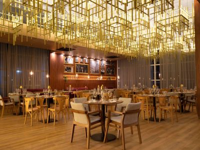 restaurante italiano exclusivo do Tauá ornamentado com luminárias contemporâneas douradas, quadros em preto e branco na parede e mesas postas em espaço amplo com grandes janelas.